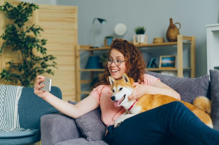 a woman sitting on a couch holding a dog and taking a selfie