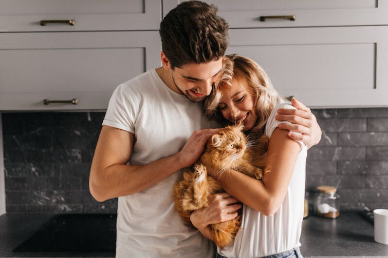 a man and woman hugging a cat in a kitchen